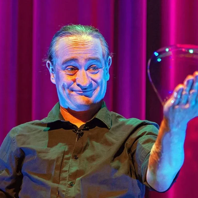Zeepbelkunstenaar Stephan Masur met handzeepbel Een man houdt een zeepbel in zijn hand en lacht tegen een kleurrijke achtergrond.