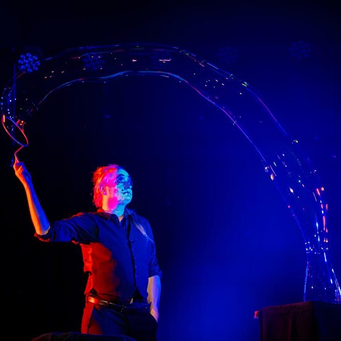 Magische bellenblaas show op bedrijfsevenement Iemand creëert een grote zeepbel op een podium voor een publiek.