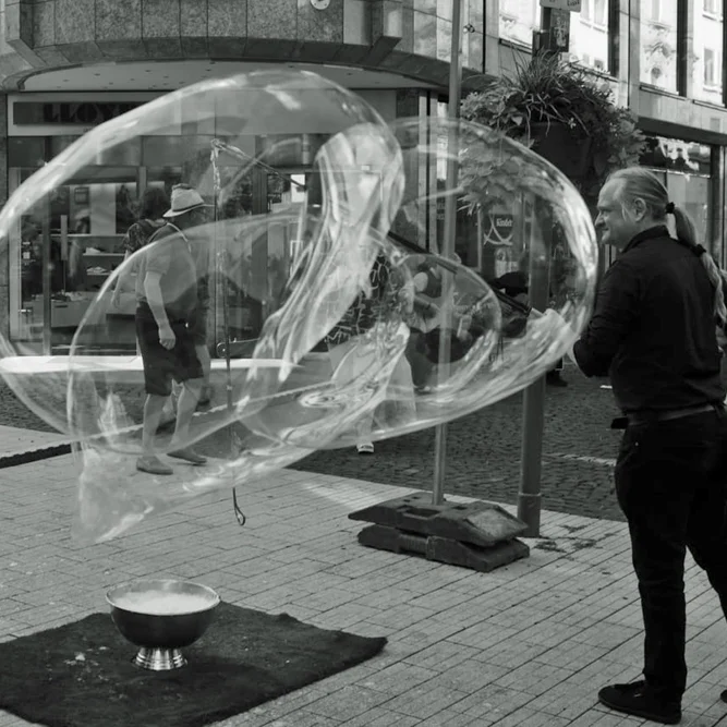 Een man blaast grote zeepbellen op een drukke straat.