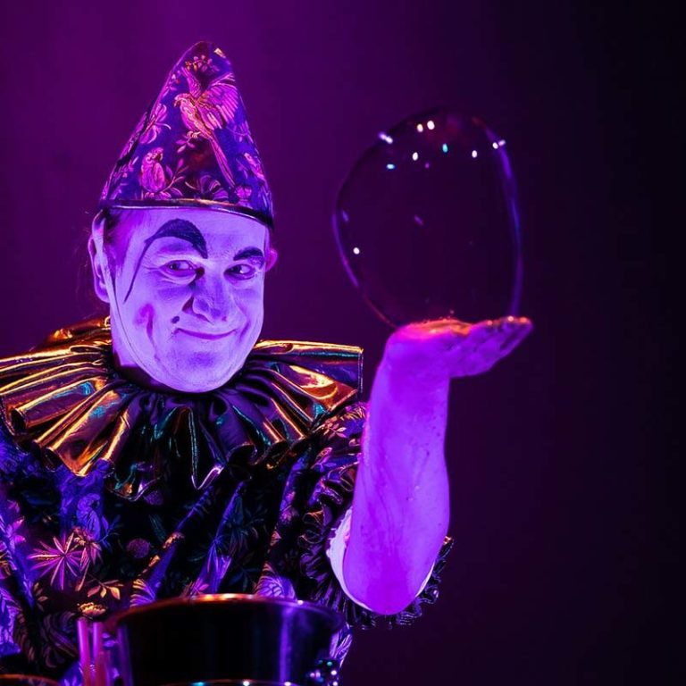 zeepbelclown met handzeepbel Clown in feestelijk tenue houdt een glinsterende zeepbel in zijn hand.